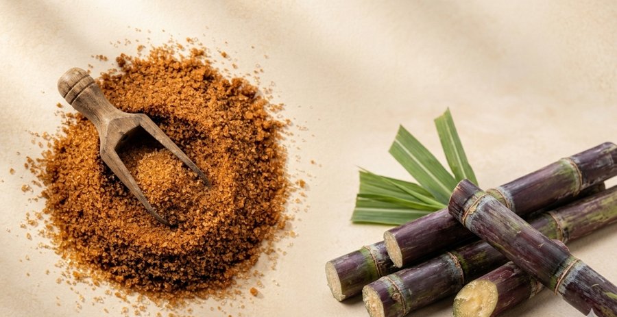 Natural jaggery powder with a wooden scoop beside fresh sugarcane